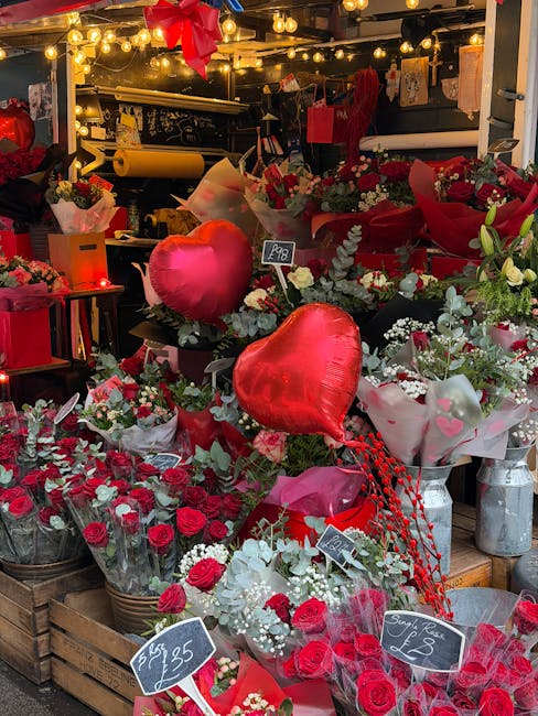 A display of fresh floral arrangements at a flower shop, featuring a variety of red and white roses, some wrapped in pink and white paper. Prominent in the foreground are two large, red heart-shaped b